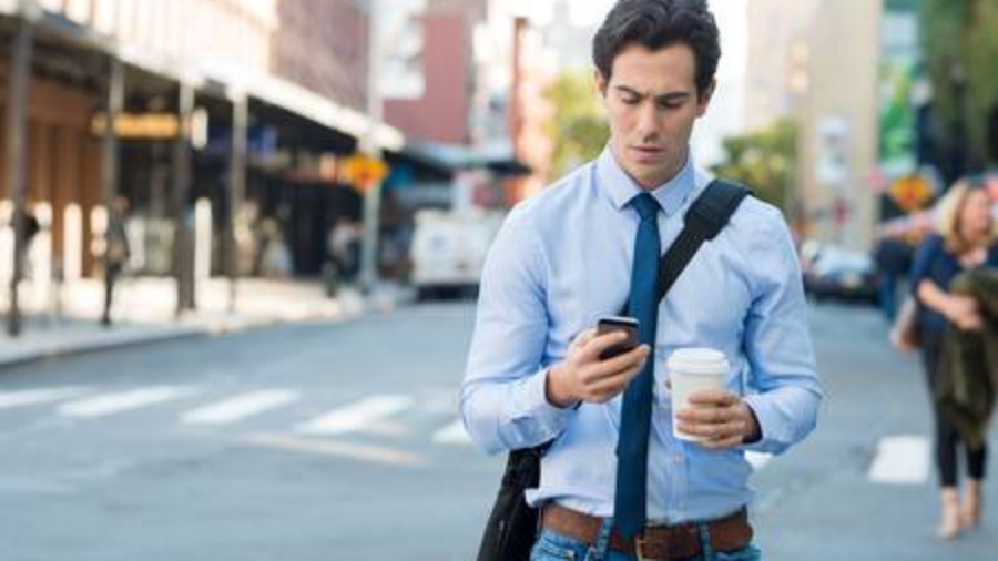 50076694 - businessman using smartphone and holding paper cup ina urban scene. worried businessman in walking on the road and messaging with phone. young man text messaging through cell phone while walking on the road in the city centre.