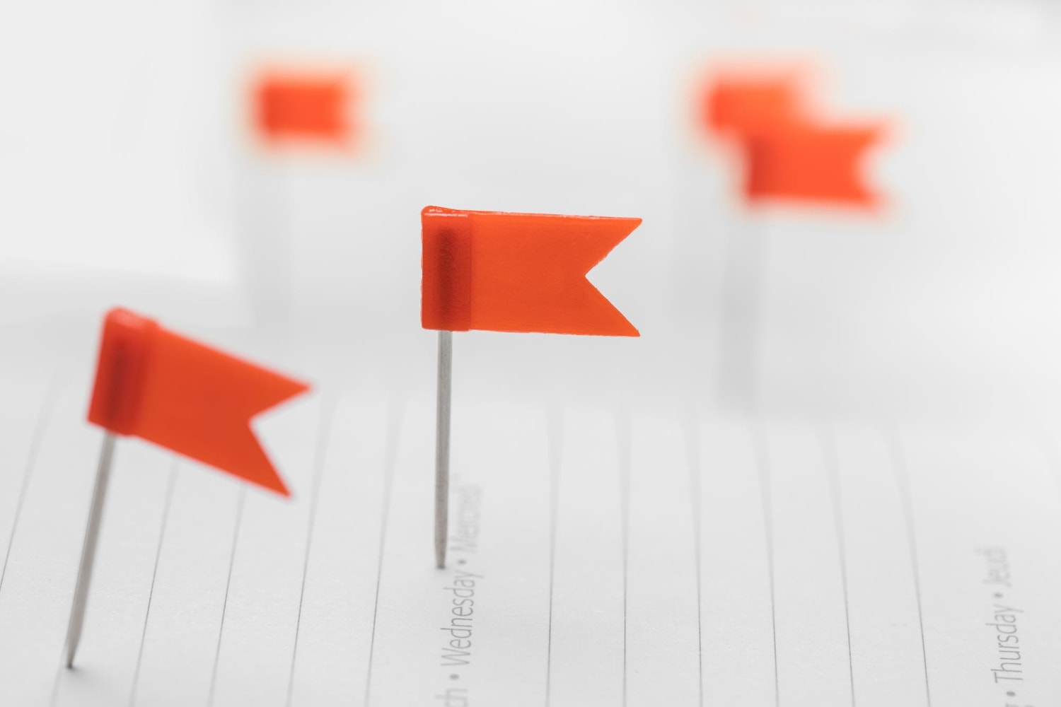 A close-up of small red flag markers pinned into a white planner or notebook, symbolizing important tasks, milestones, or reminders.