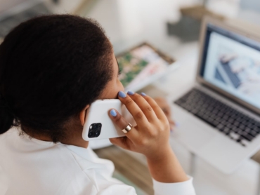 Woman holding smartphone to ear while working on a laptop. Modern communication and multitasking.