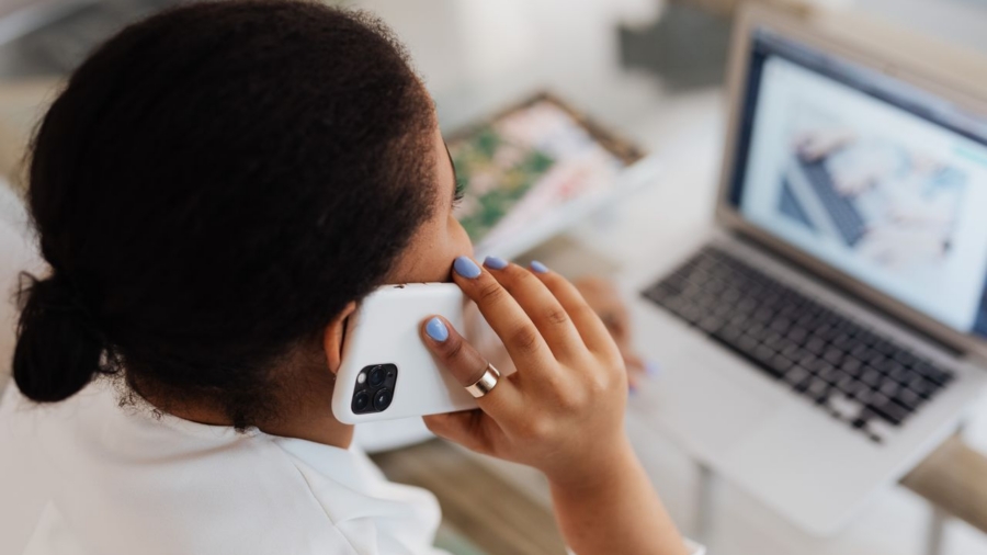 Woman holding smartphone to ear while working on a laptop. Modern communication and multitasking.