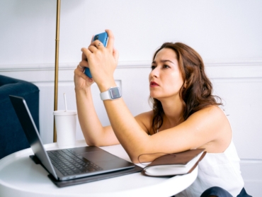 Woman multitasking at home with phone and laptop, appearing focused and engaged.