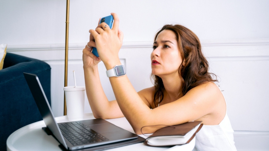 Woman multitasking at home with phone and laptop, appearing focused and engaged.